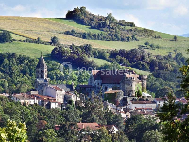 Village avec église romane et château médiéval entourés de collines verdoyantes sous un ciel clair.