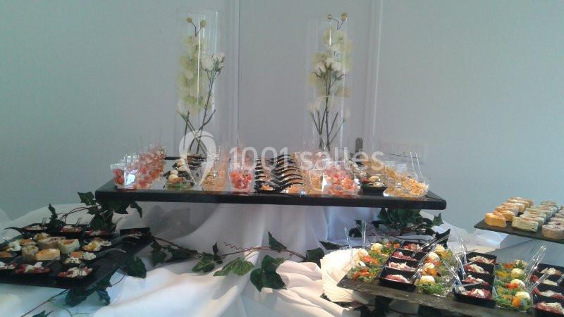Buffet élégant avec verrines colorées, petits plats variés et décoration florale blanche sur nappes blanches.