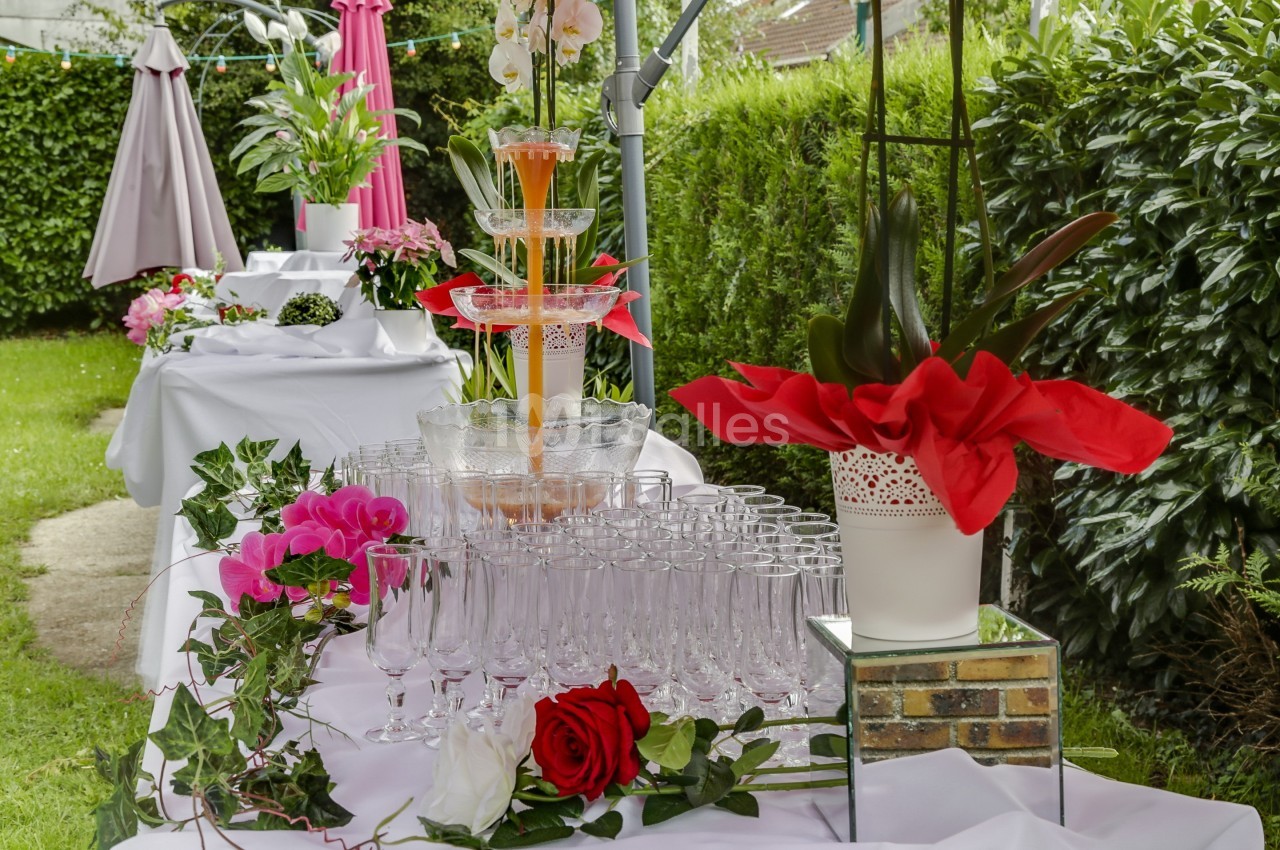 Fontaine à cocktails entourée de verres et de décorations florales sur une table dressée dans un jardin.