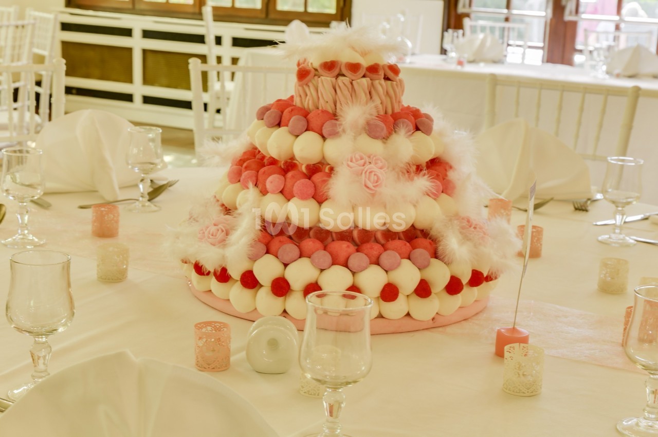 Pièce montée décorative en bonbons roses et blancs, disposée sur une table dressée avec des verres et des bougies.