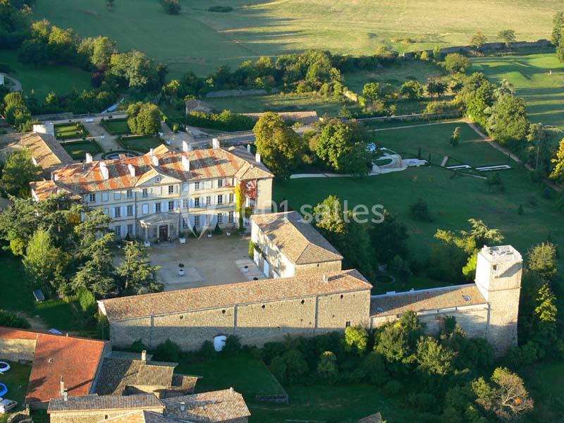 Vue aérienne d'un château entouré de jardins et de verdure, avec des bâtiments en pierre et des toits en tuiles.