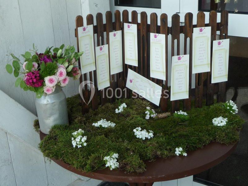 Arrangement floral avec un bouquet de roses dans un vase et un panneau en bois affichant des cartes sur une table décorée de…