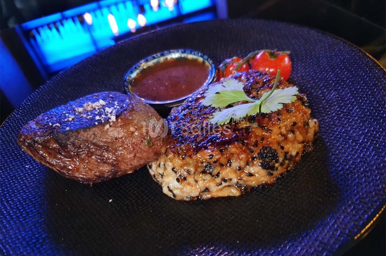 Assiette avec un steak, un accompagnement de riz grillé garni de coriandre, une sauce et des tomates cerises.