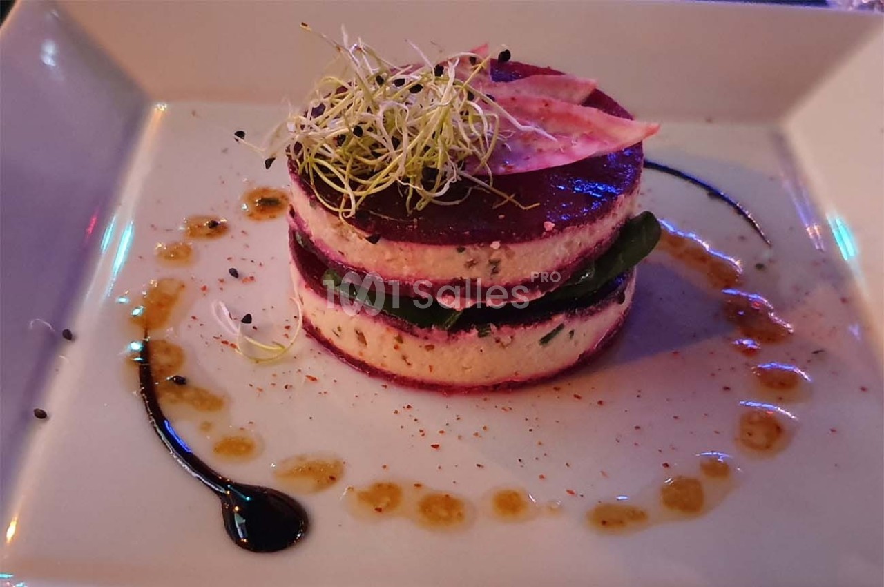 Entrée végétarienne dressée en millefeuille avec betterave, fromage et pousses, entourée de sauces décoratives.
