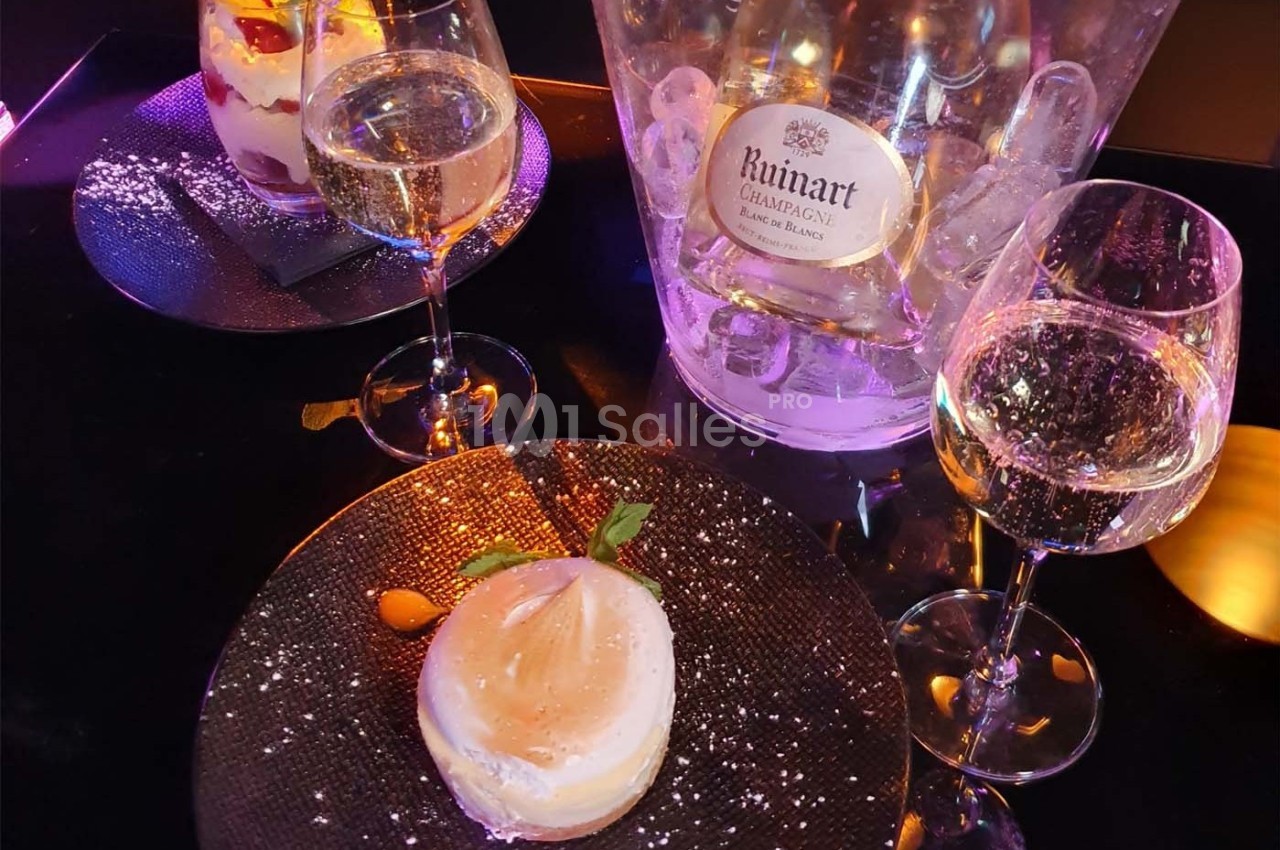 Deux verres de champagne, un dessert sur assiette noire et un seau à glace contenant une bouteille de Ruinart.