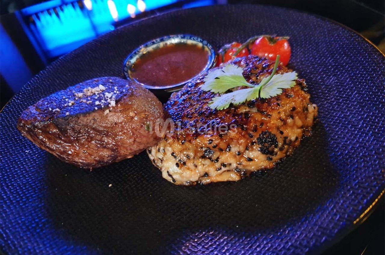 Assiette contenant un steak grillé, une pomme de terre rôtie, une sauce et des tomates cerises en garniture.