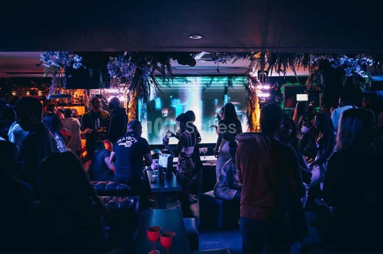 Personnes rassemblées dans un bar ou club animé, éclairé par des lumières colorées et une ambiance festive.