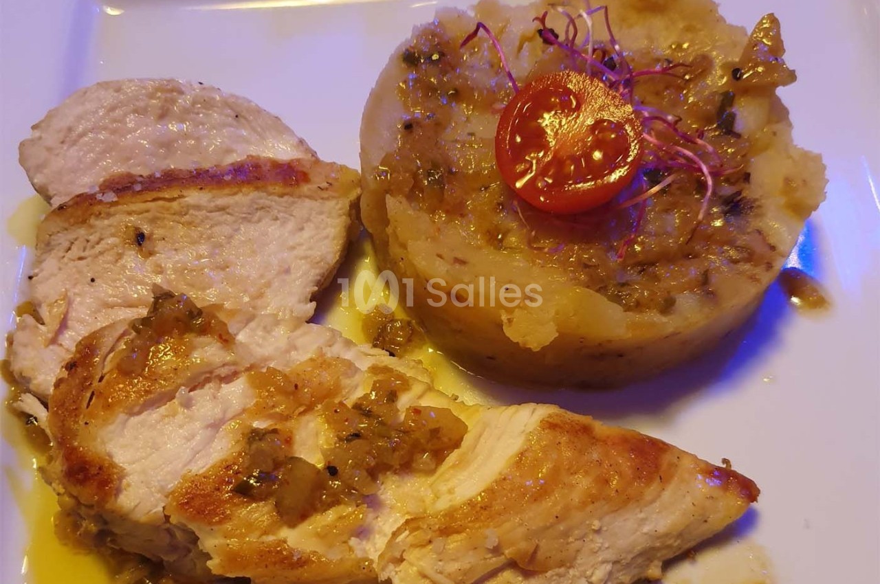 Assiette contenant des filets de poulet grillés et une purée garnie d'oignons caramélisés et d'une tomate cerise.