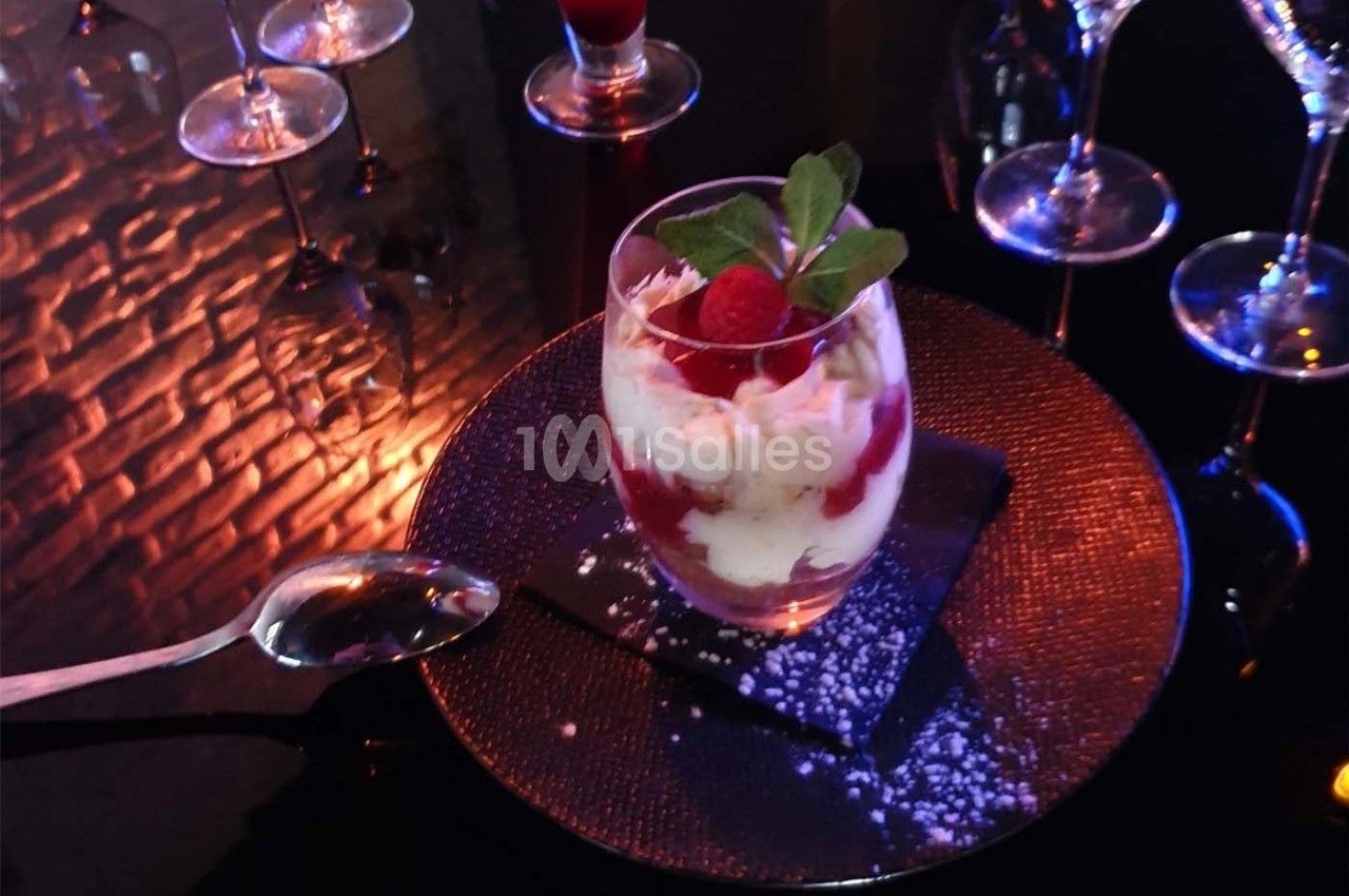Verrine de dessert avec crème, coulis de fruits rouges, framboise et menthe, servie sur une assiette noire.