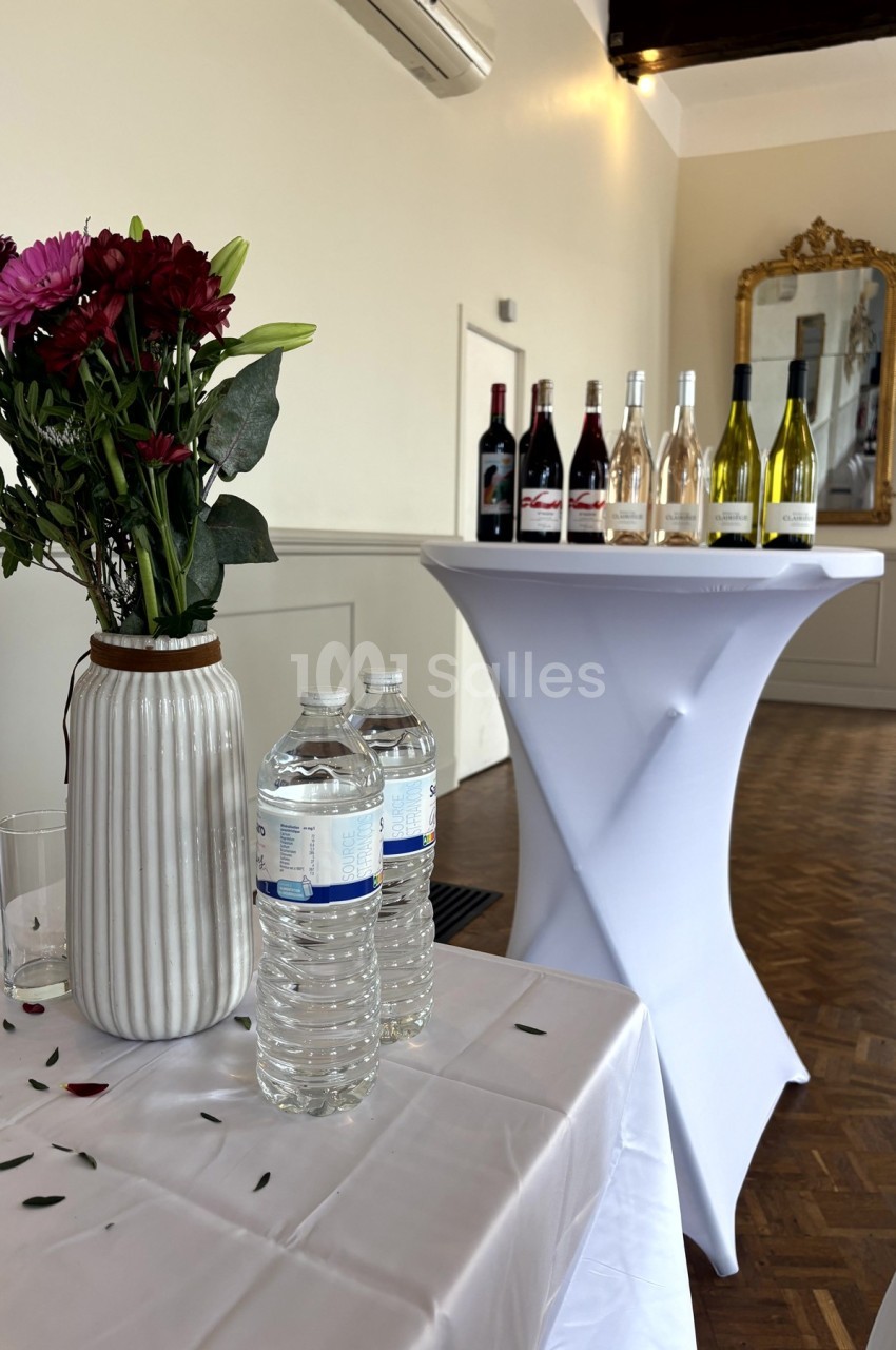 Vase de fleurs, bouteilles d'eau et assortiment de vins sur des tables dans une salle lumineuse avec miroir mural.