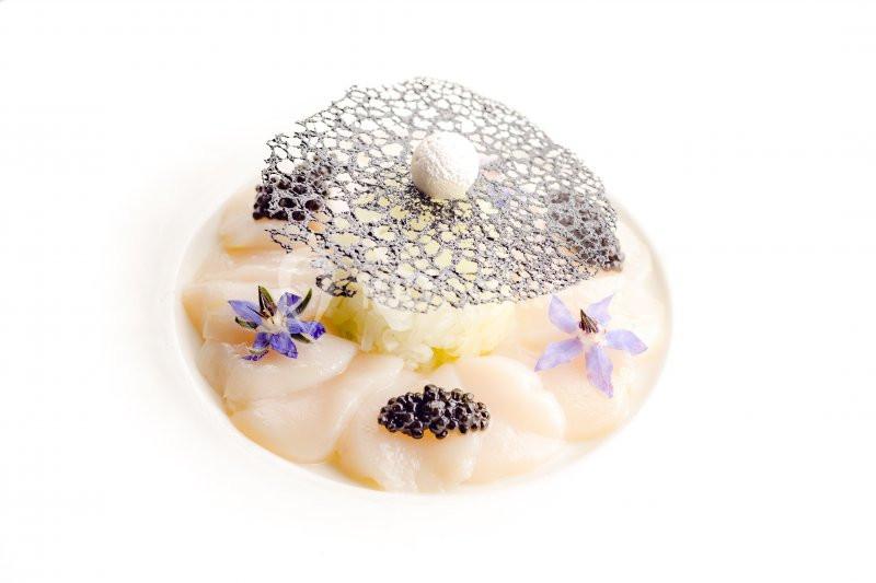 Assiette gastronomique avec carpaccio de coquilles Saint-Jacques, caviar, fleurs comestibles et décoration en dentelle noire.