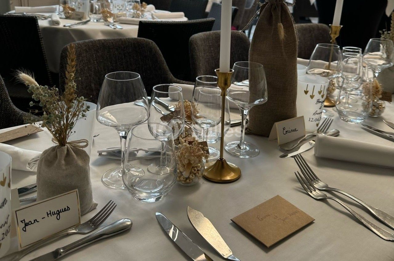 Table élégamment dressée avec vaisselle, bougies dorées, fleurs séchées et marque-places personnalisés.