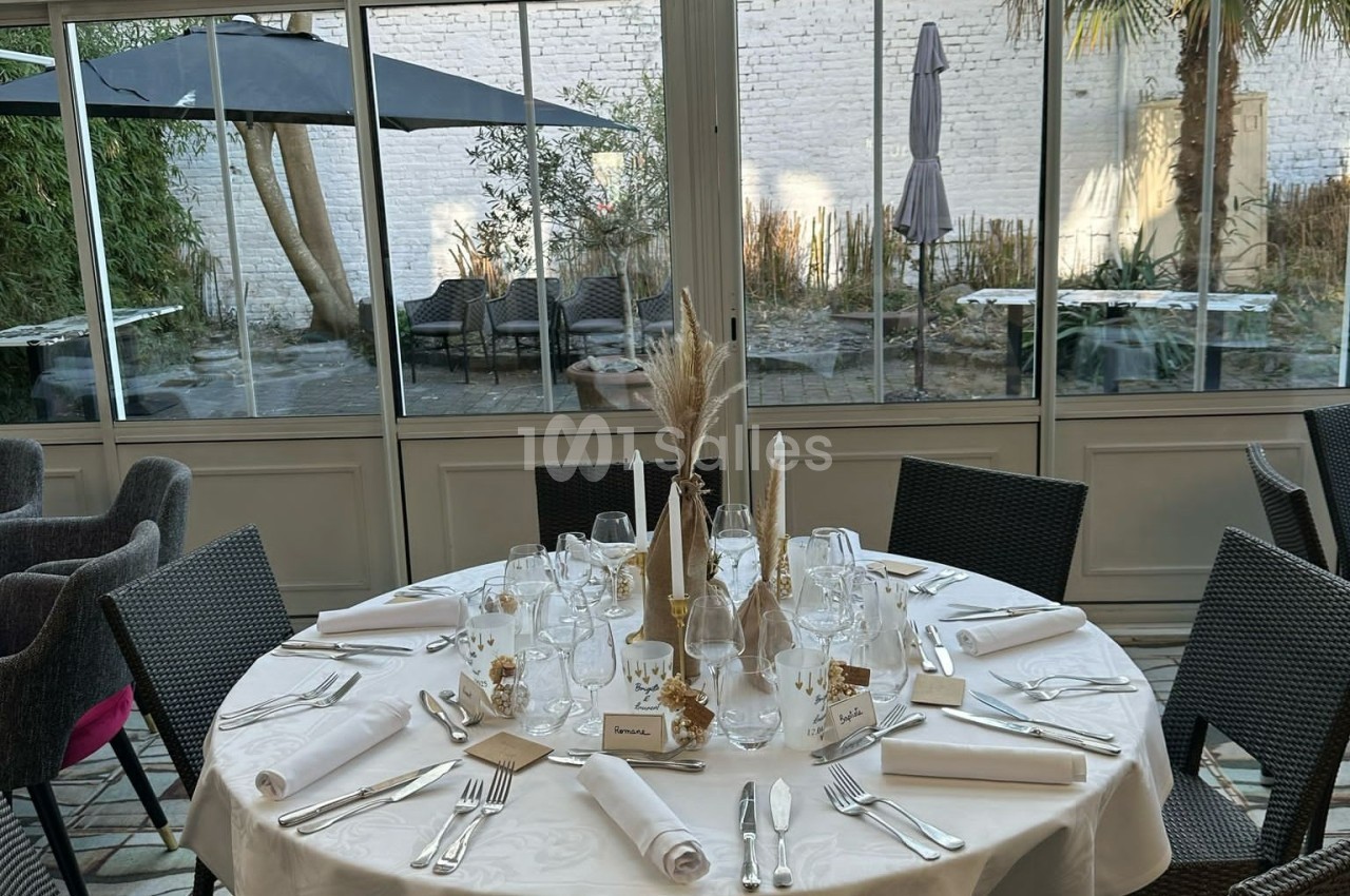 Table élégamment dressée avec nappes blanches, couverts, verres et décorations, dans une salle lumineuse avec vue sur un…