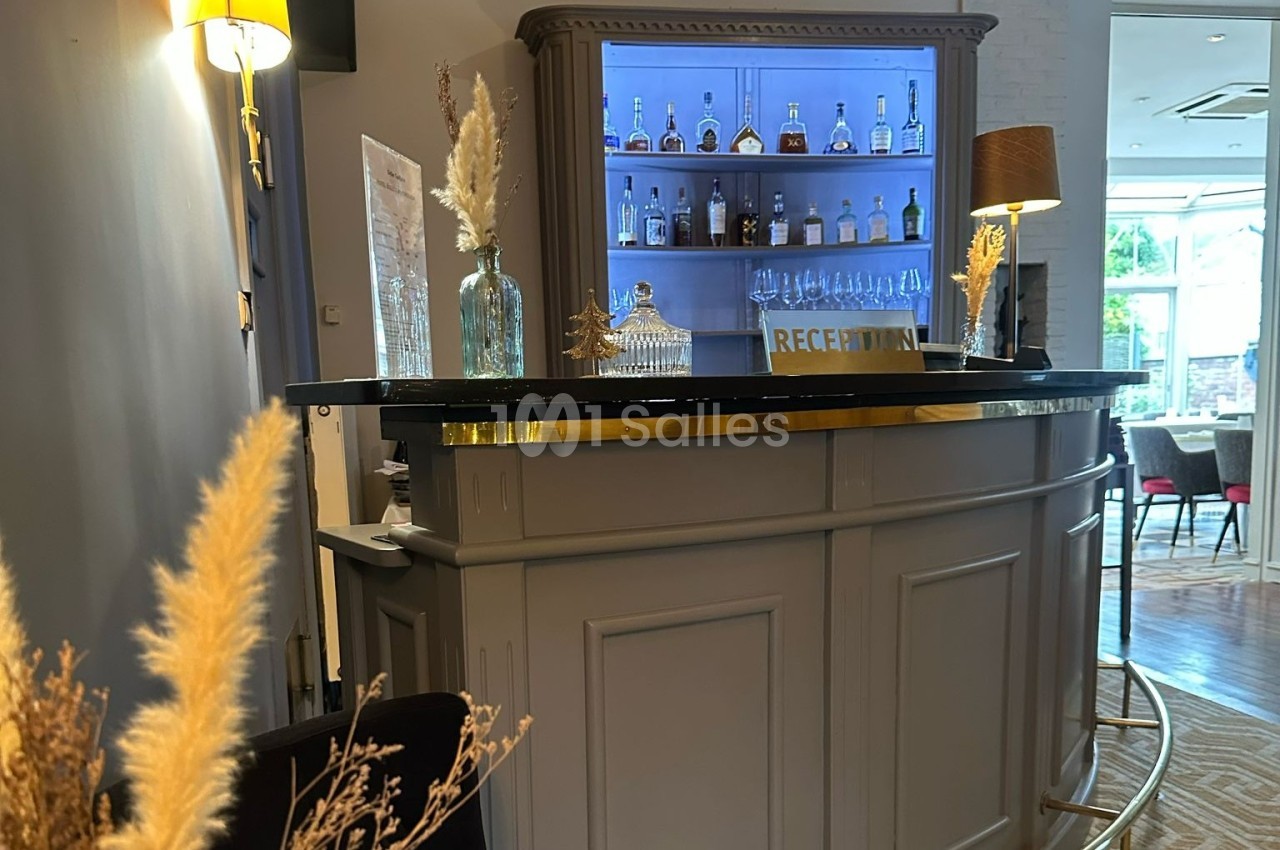 Comptoir de réception en bois avec étagères éclairées contenant des bouteilles et des verres, décoré de plantes séchées.