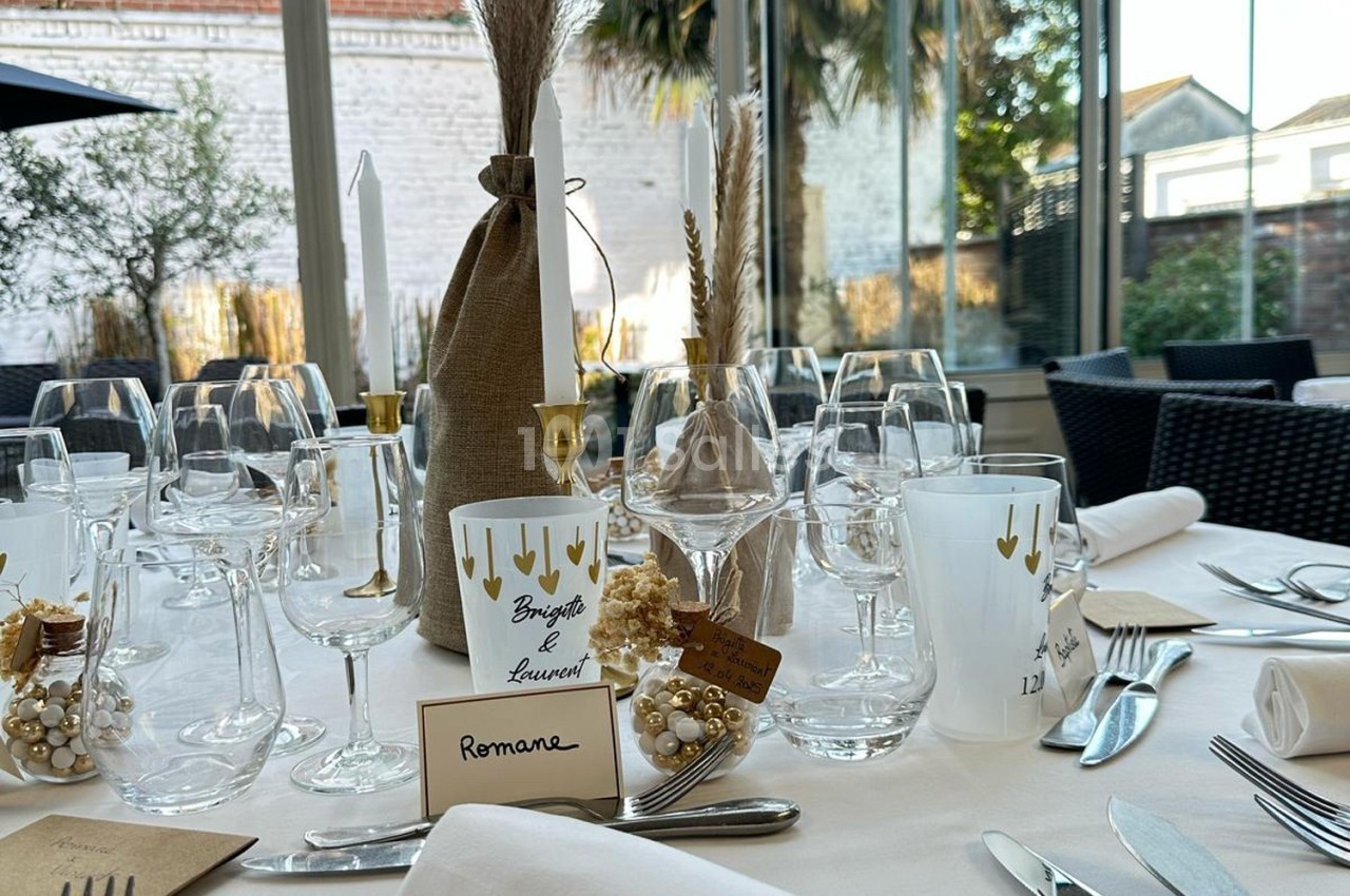 Table élégamment dressée avec des verres, bougies décorées, marque-places et ornements dorés dans une salle lumineuse.