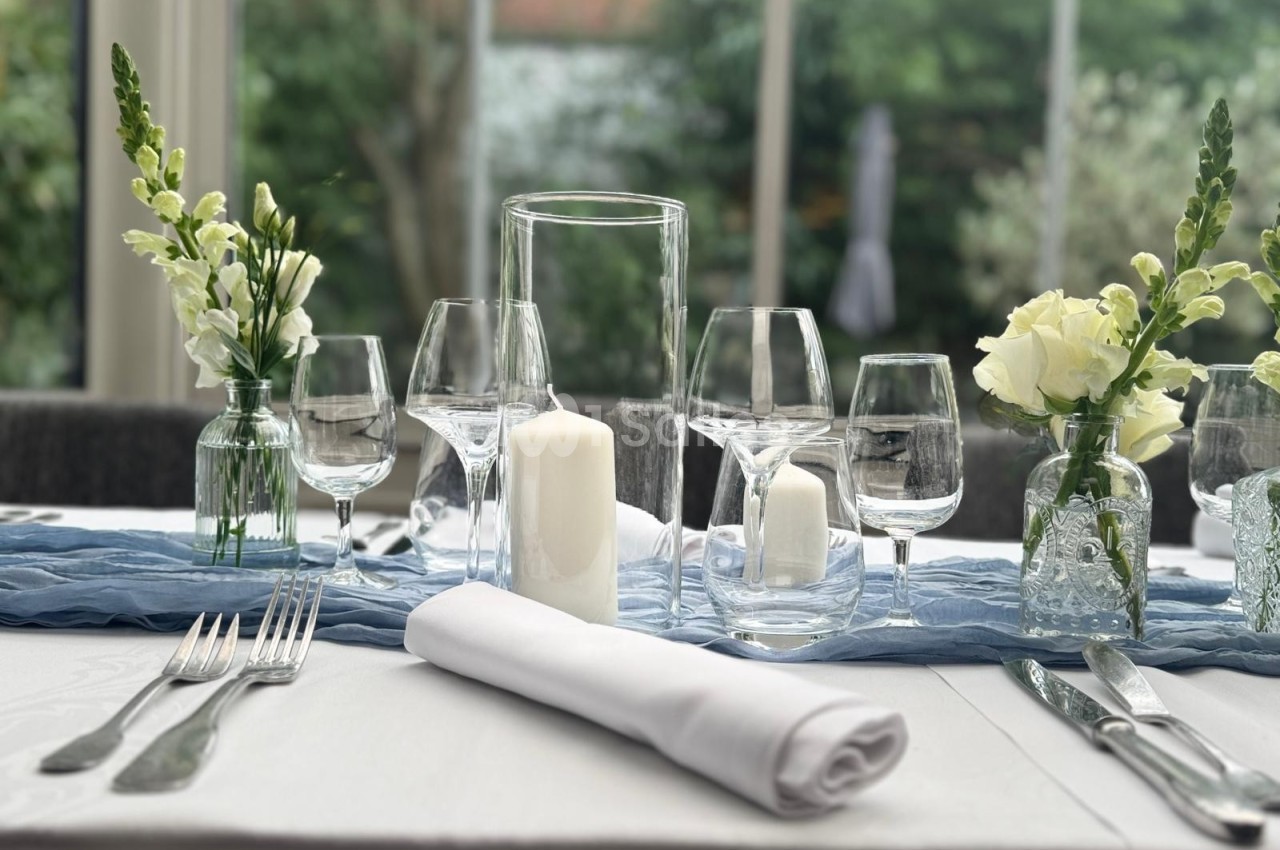 Table élégamment dressée avec verres, couverts, bougie blanche et petits bouquets de fleurs dans un cadre lumineux.