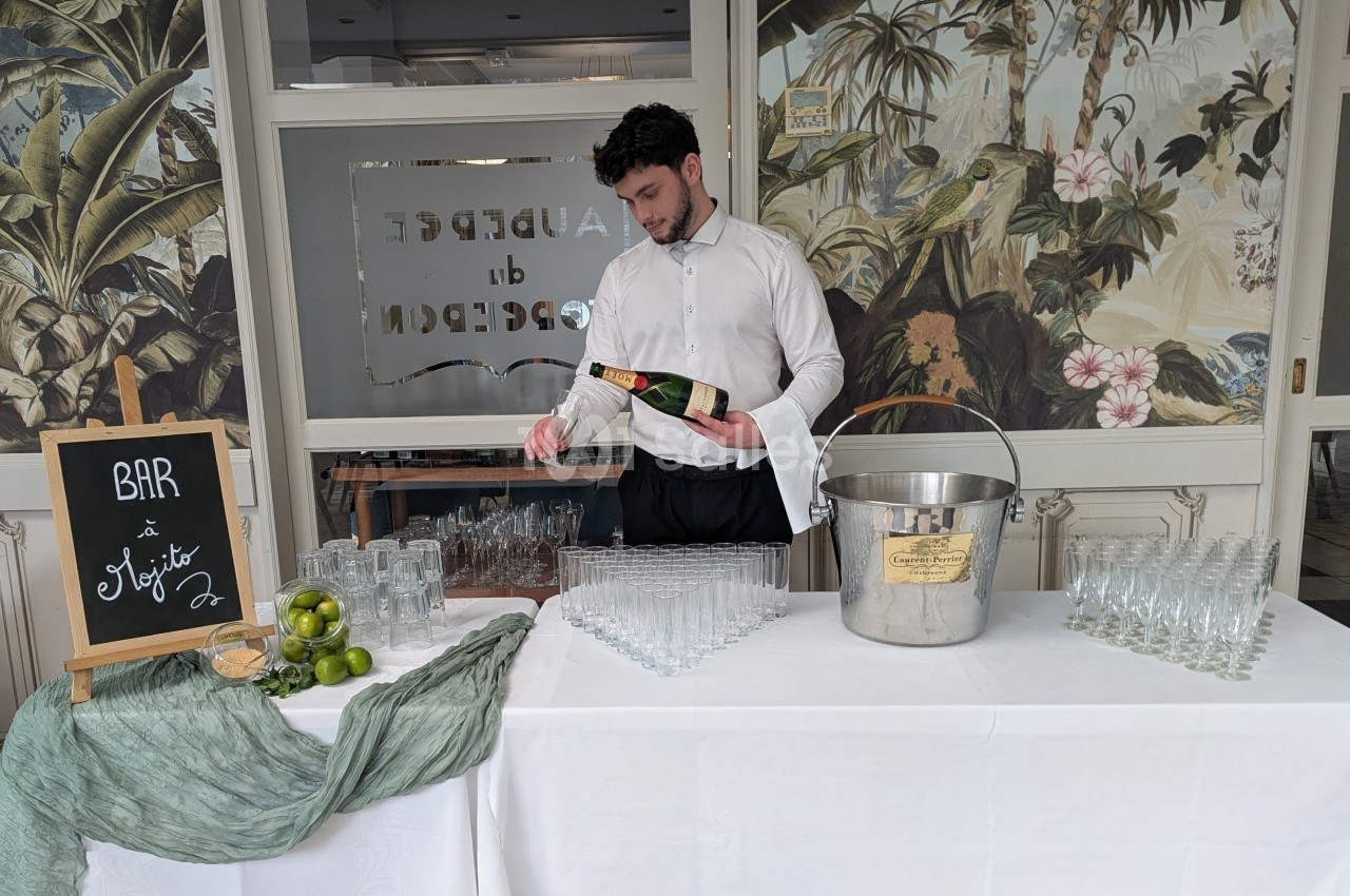 Serveur versant une boisson dans un verre sur une table dressée avec des verres, des citrons et un seau à glace.