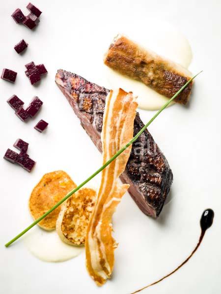 Assiette gastronomique composée de viande grillée, légumes en cubes, chips croustillante et sauce décorative.