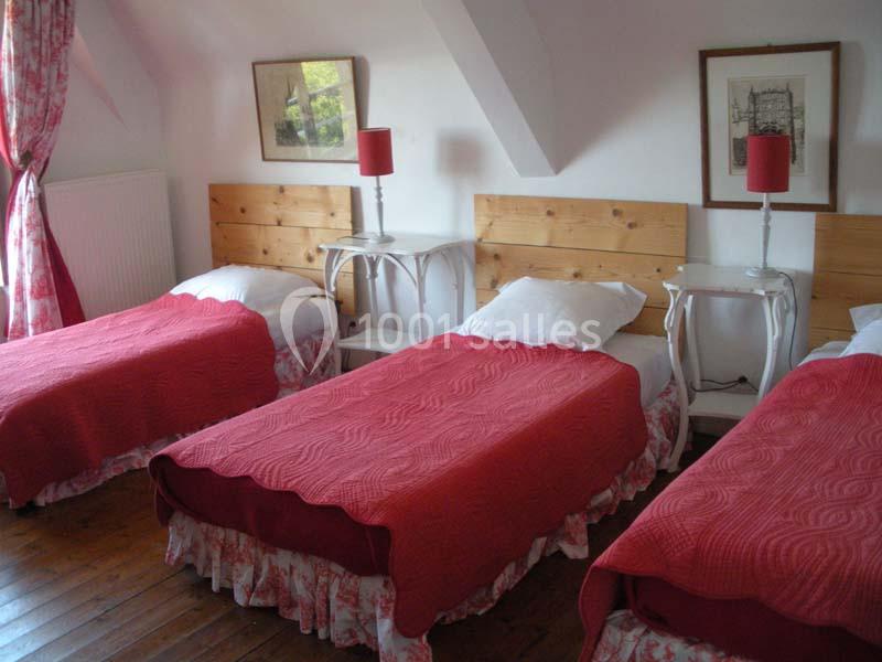 Trois lits simples avec couvre-lits rouges dans une chambre lumineuse, décorée de meubles en bois et de lampes assorties.
