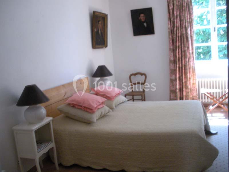 Chambre simple avec un lit double, deux lampes de chevet, des tableaux au mur et une grande fenêtre avec rideaux.