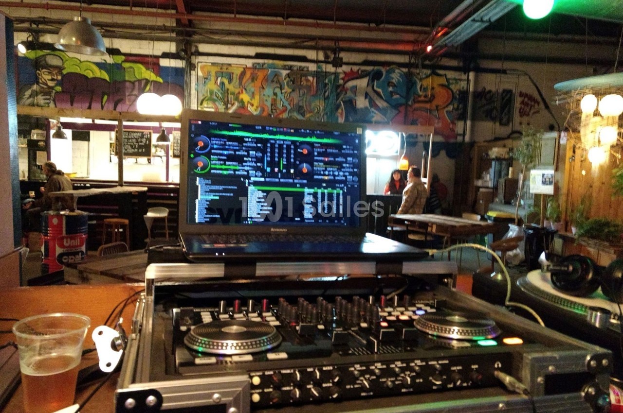 Poste de DJ avec platines et ordinateur affichant un logiciel musical, dans un espace décoré de graffitis.