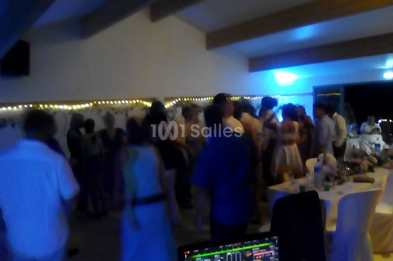 Groupe de personnes dans une salle éclairée, dansant et discutant lors d'un événement festif en soirée.