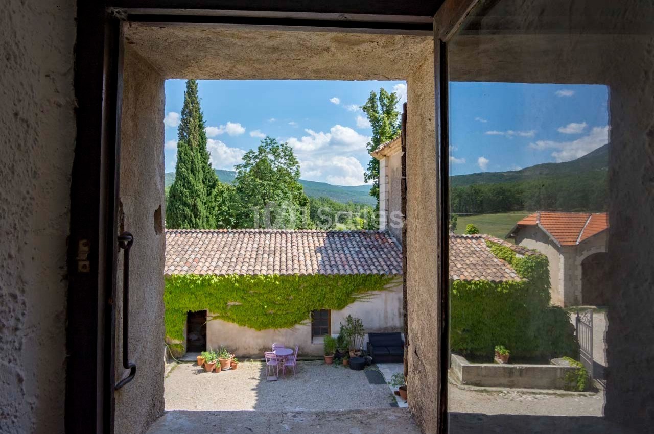 Vue depuis une fenêtre sur une cour intérieure avec des murs recouverts de lierre, des meubles de jardin et un paysage…