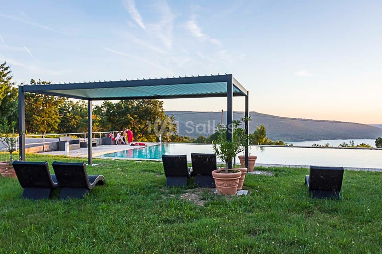 Pergola moderne près d'une piscine à débordement avec vue sur des collines au coucher du soleil.