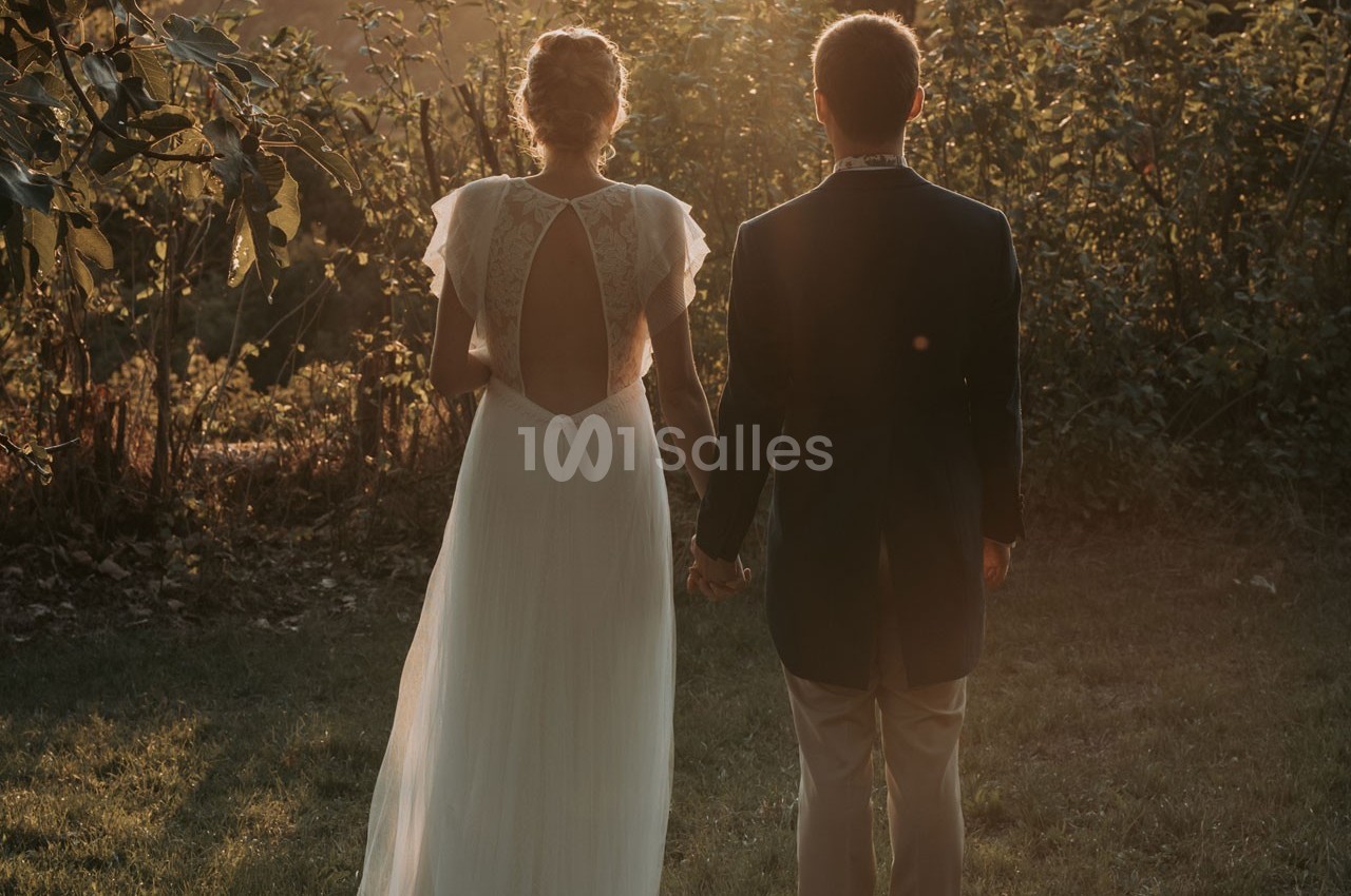 Un couple de dos, tenant la main, vêtu élégamment, dans un jardin au coucher du soleil.