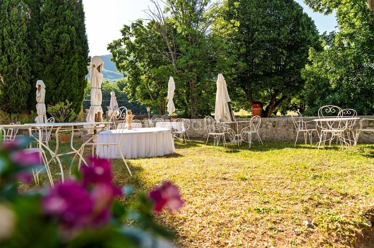 Mobilier de jardin en fer forgé disposé sur une pelouse ensoleillée, entouré d'arbres et de parasols fermés.