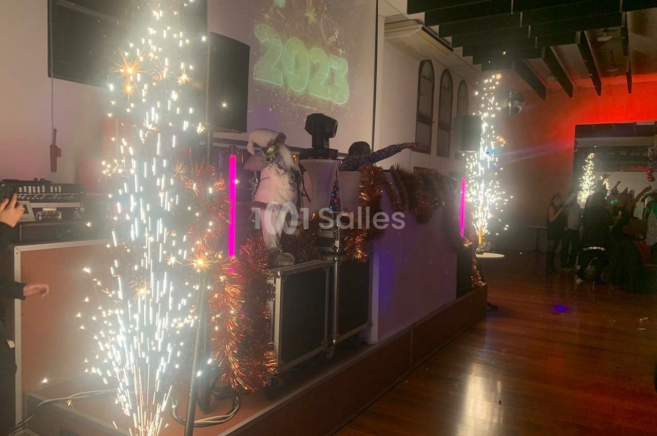 Scène festive avec DJ, décorations lumineuses, étincelles et projection de ’2023’ dans une salle animée.