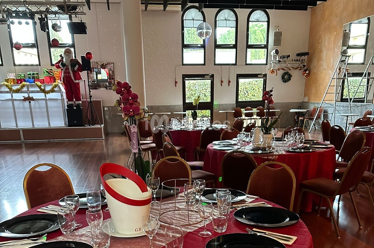 Salle de réception décorée avec des tables dressées, des nappes rouges, des orchidées et une scène en arrière-plan.
