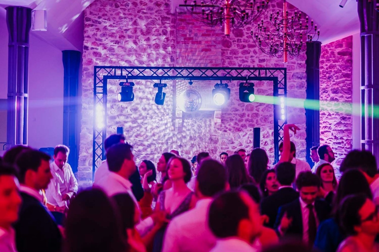 Groupe de personnes dansant sous des lumières colorées dans une salle en pierre avec un éclairage de fête.