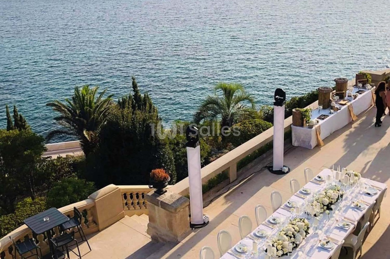 Table décorée pour un événement en extérieur, avec vue sur la mer, des palmiers et une terrasse élégante.
