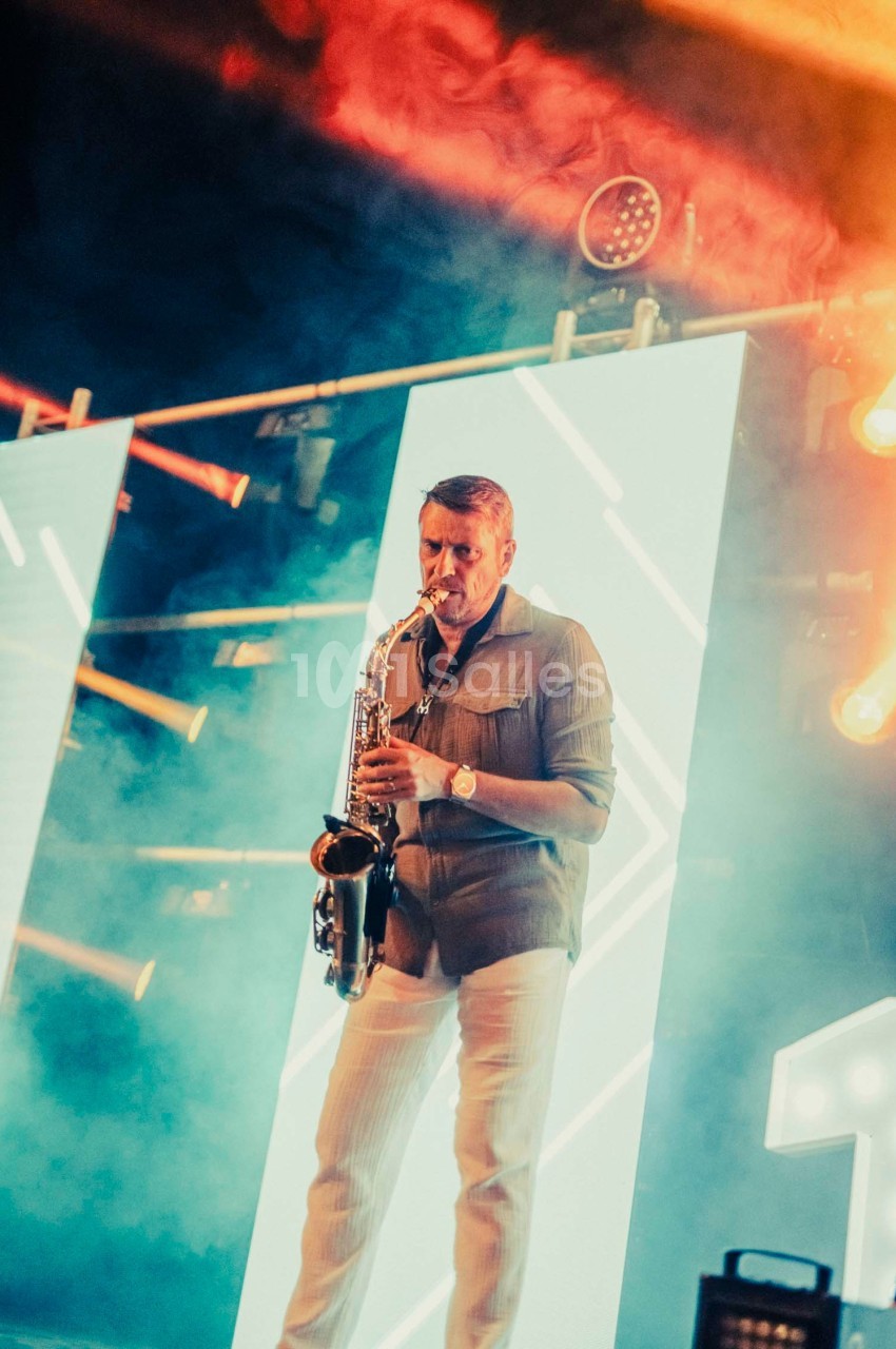 Un musicien joue du saxophone sur une scène illuminée par des panneaux lumineux et des projecteurs colorés.