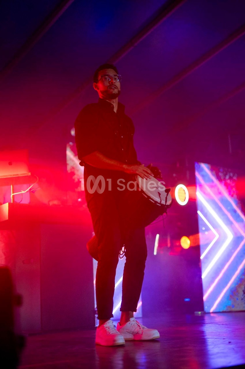 Un musicien joue du tambourin sur une scène éclairée par des lumières rouges et bleues.