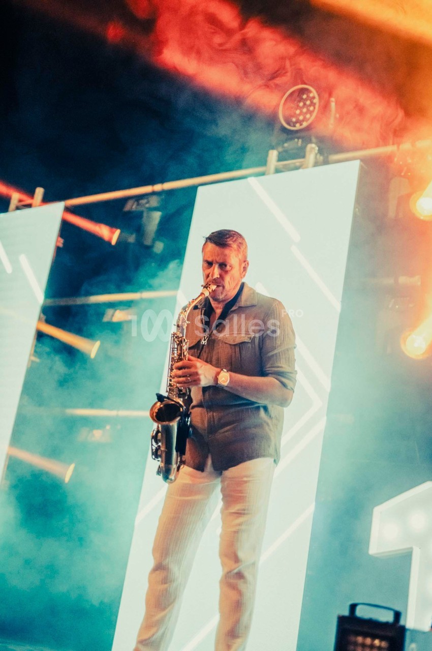 Un musicien joue du saxophone sur une scène illuminée par des panneaux lumineux et des projecteurs colorés.