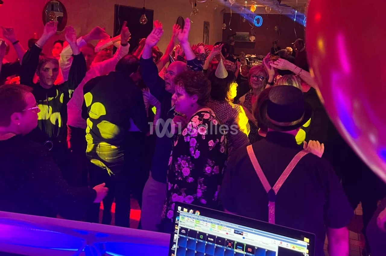Groupe de personnes dansant sous des lumières colorées lors d'une soirée festive en intérieur.