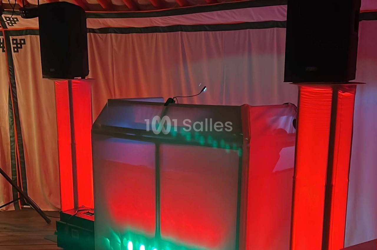 Un pupitre éclairé en rouge et vert, entouré de haut-parleurs noirs, dans une salle avec rideaux blancs.