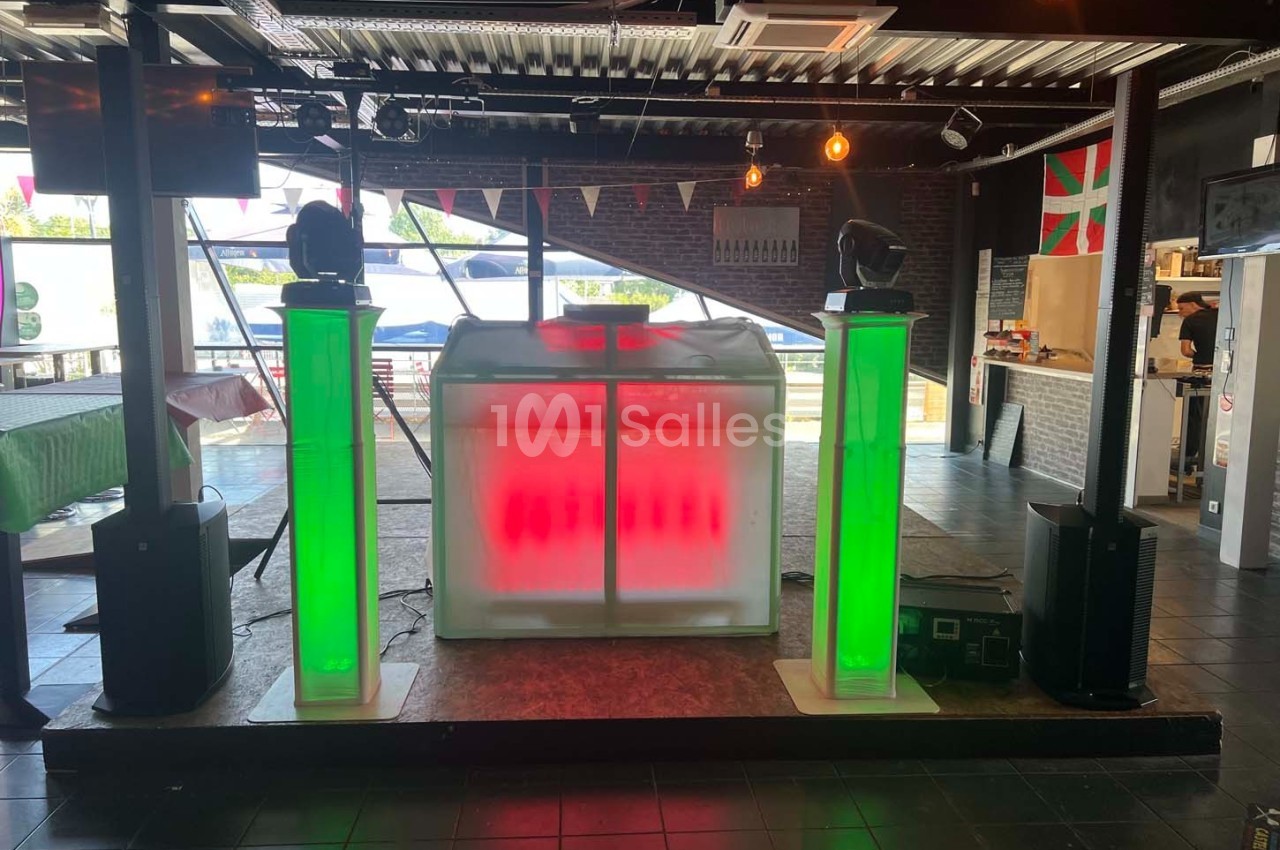Stand de DJ avec éclairage LED rouge et vert, installé dans une salle avec décoration intérieure et lumière naturelle.