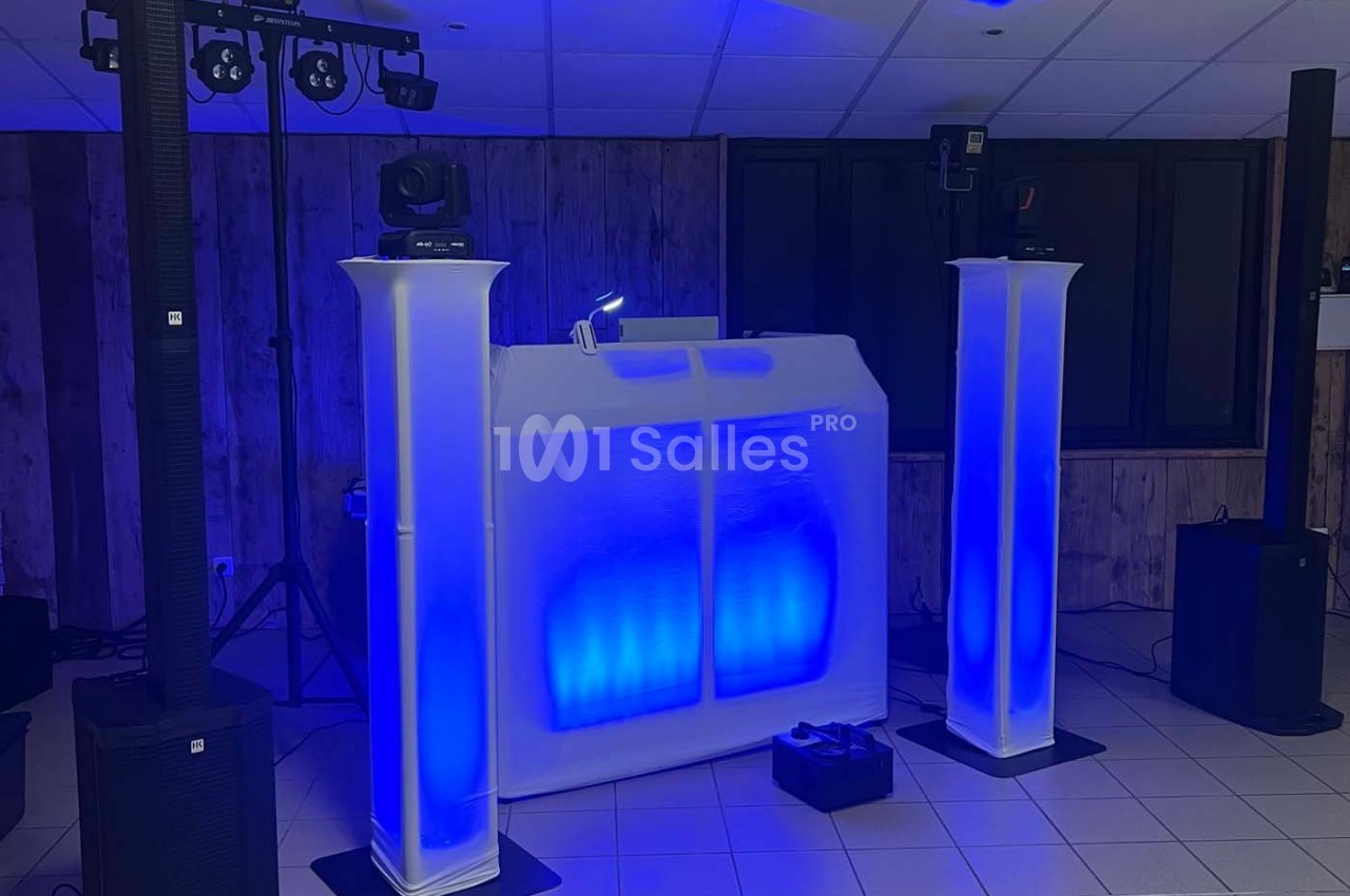 Poste de DJ éclairé en bleu avec deux colonnes lumineuses, matériel audio et projecteurs dans une salle.