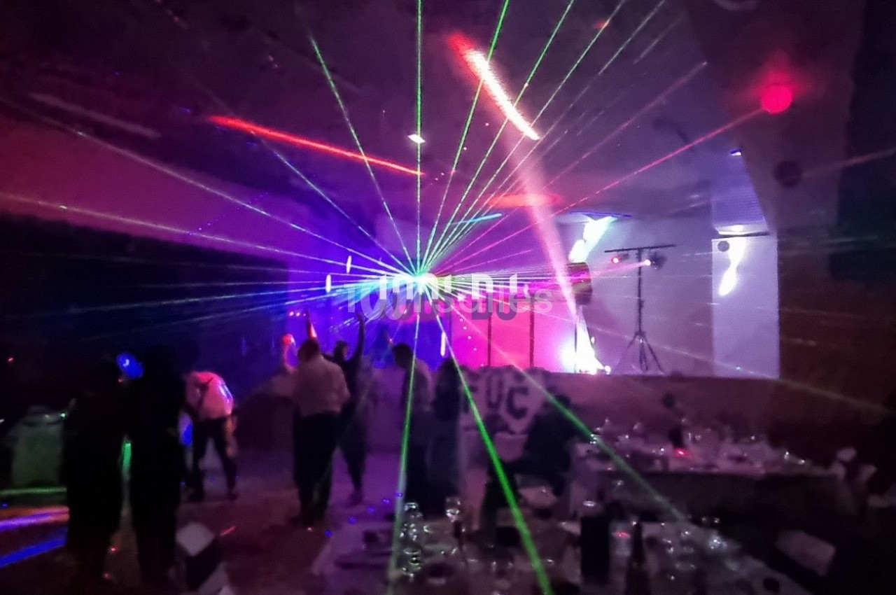 Salle sombre avec des jeux de lumière laser colorés et des silhouettes de personnes dans une ambiance festive.