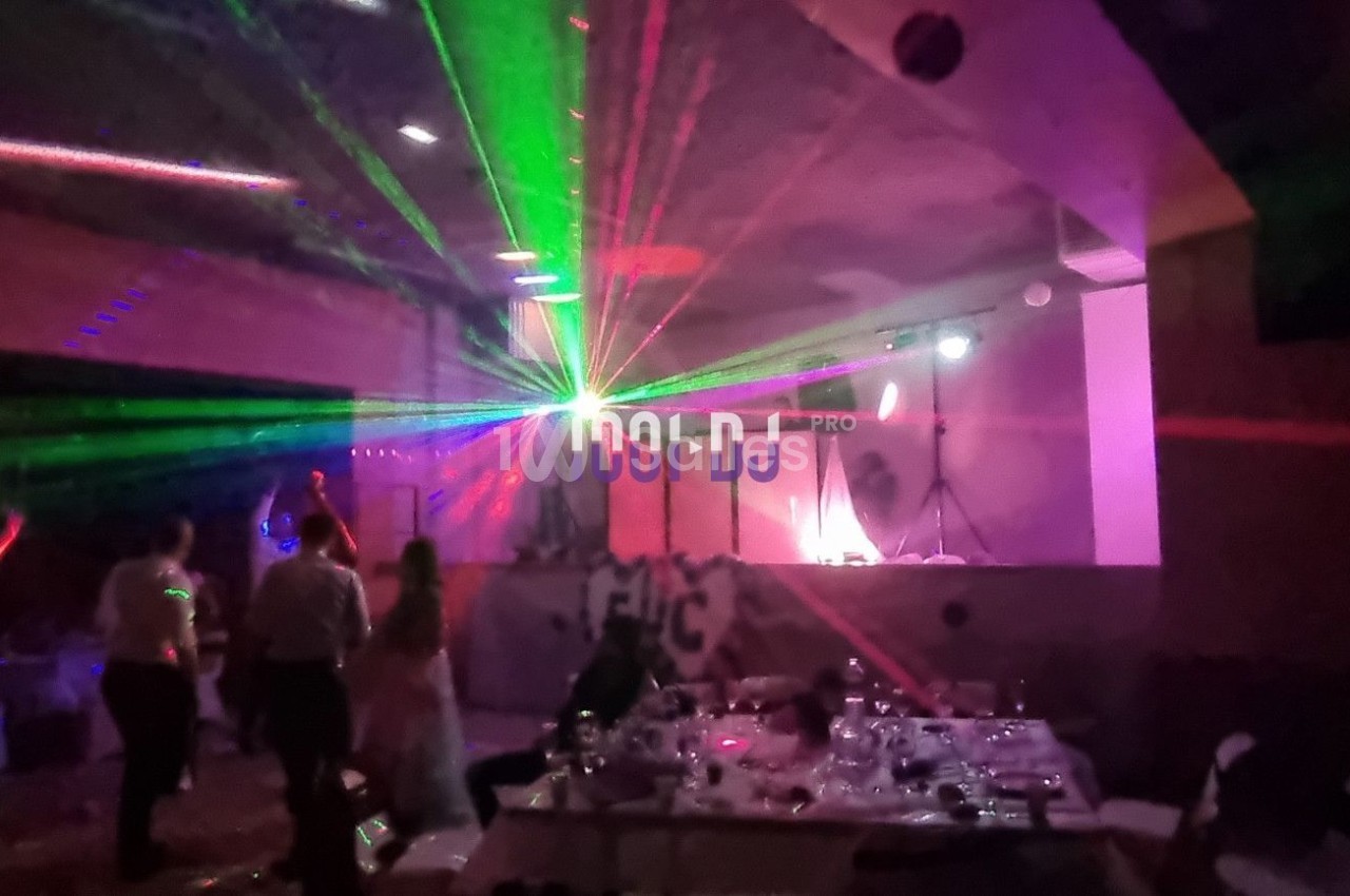 Salle de fête avec des jeux de lumière colorés, une piste de danse et des invités debout ou assis.