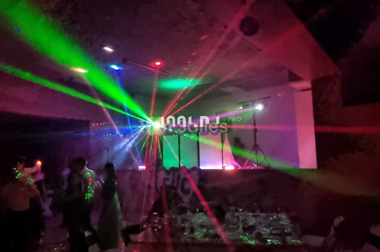 Salle sombre avec des jeux de lumières colorées et des personnes dansant sous des faisceaux laser.