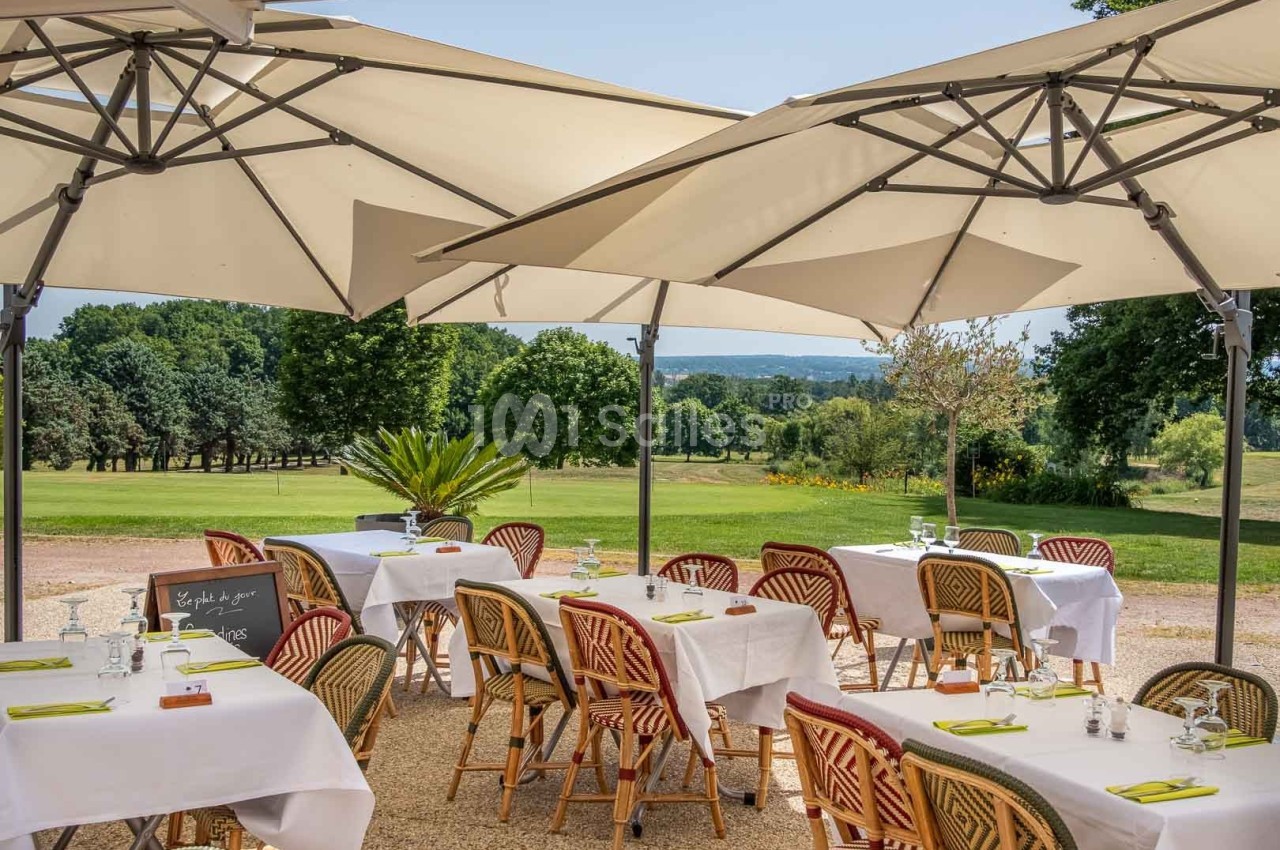 Terrasse d'un restaurant avec tables dressées sous des parasols, offrant une vue sur un paysage verdoyant.