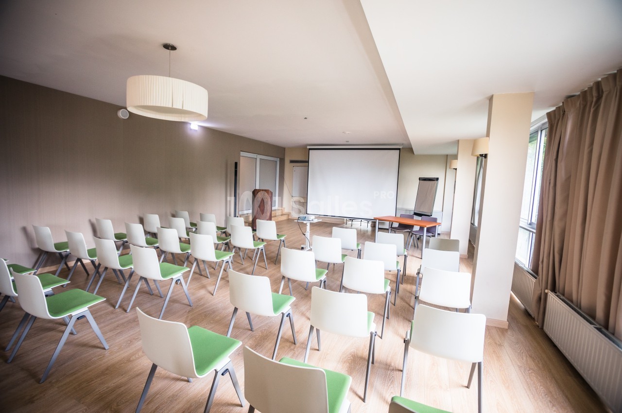 Salle de réunion lumineuse avec des rangées de chaises blanches et vertes, un écran de projection et un tableau de…