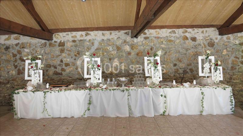 Table de réception décorée avec des fleurs blanches et rouges, ornée de guirlandes végétales, dans une salle en pierre.