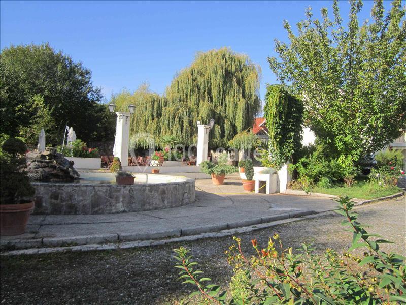 Cour extérieure avec fontaine en pierre, bancs, pots de fleurs et arbres, sous un ciel dégagé.