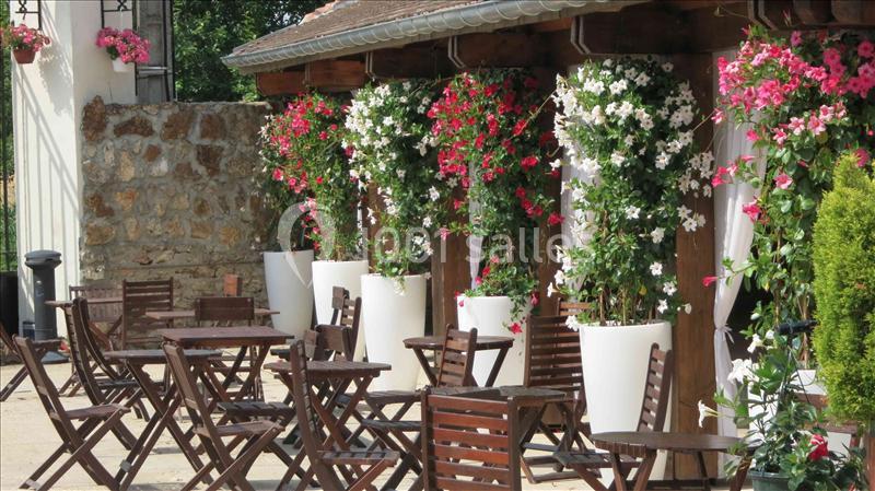 Terrasse extérieure avec tables en bois et pots de fleurs colorées disposés le long d'un mur en pierre.