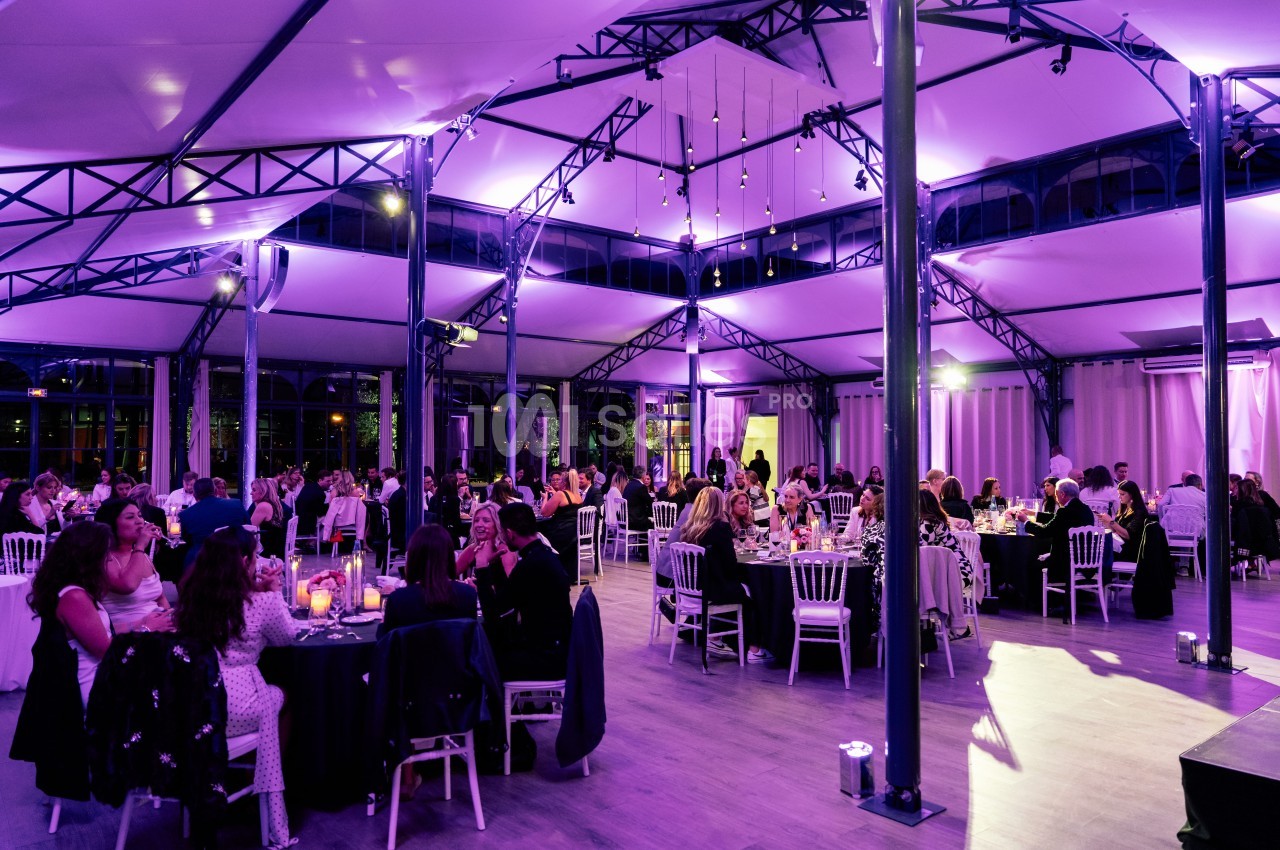 Salle de réception lumineuse avec des invités assis à des tables rondes sous un éclairage violet.